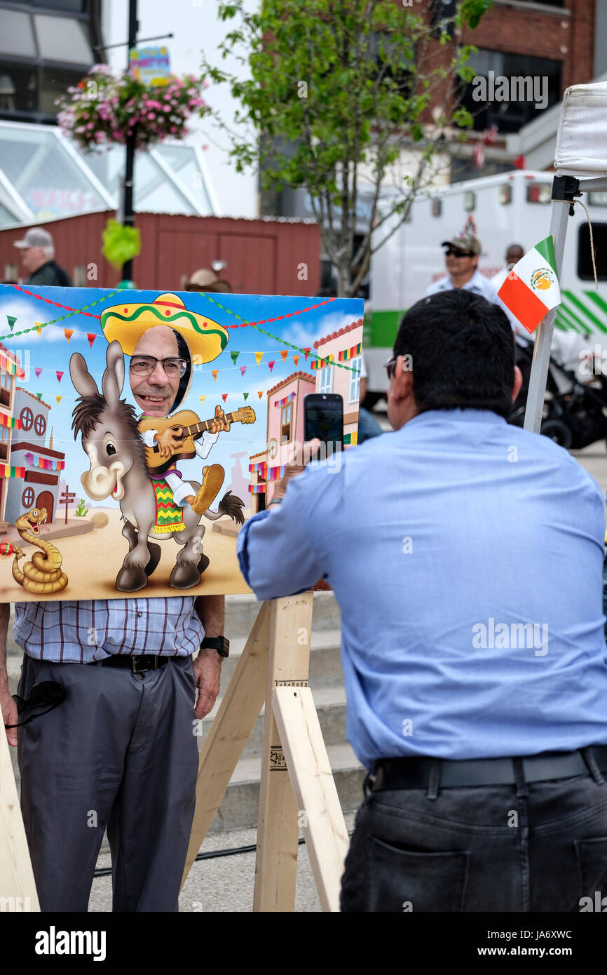 Un uomo adulto, maschio, scattare una fotografia di un amico in posa con il suo volto attraverso una peep attraverso la scheda, spioncino, scheda di foto a una festa messicana. Foto Stock