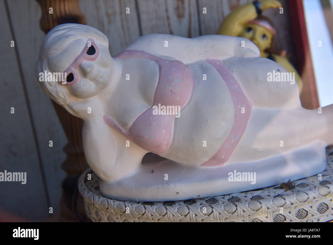Giocosa statuetta in ceramica di una donna sdraiata in bikini rosa e occhiali da sole, aggiungendo umorismo e fascino a un ambiente rustico Foto Stock