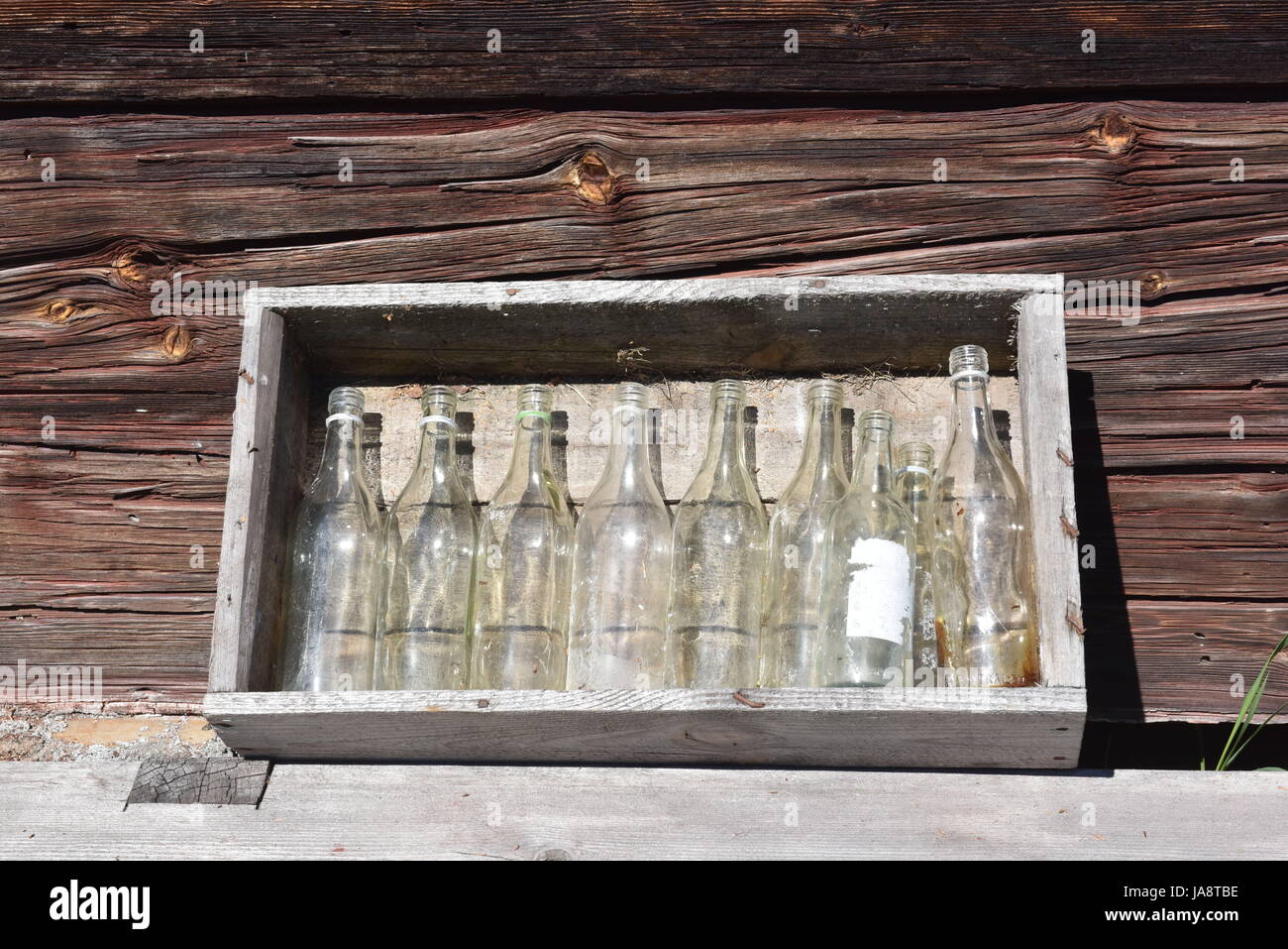 Vecchie bottiglie di vetro esposte in una cassa di legno rustica contro una parete di legno intemprata, evocando fascino vintage e semplicità rurale Foto Stock