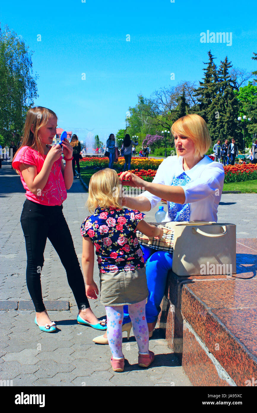 Madre corregge la figlia della capelli durante una passeggiata attraverso la città di primavera. Famiglia a piedi attraverso la città di primavera Foto Stock