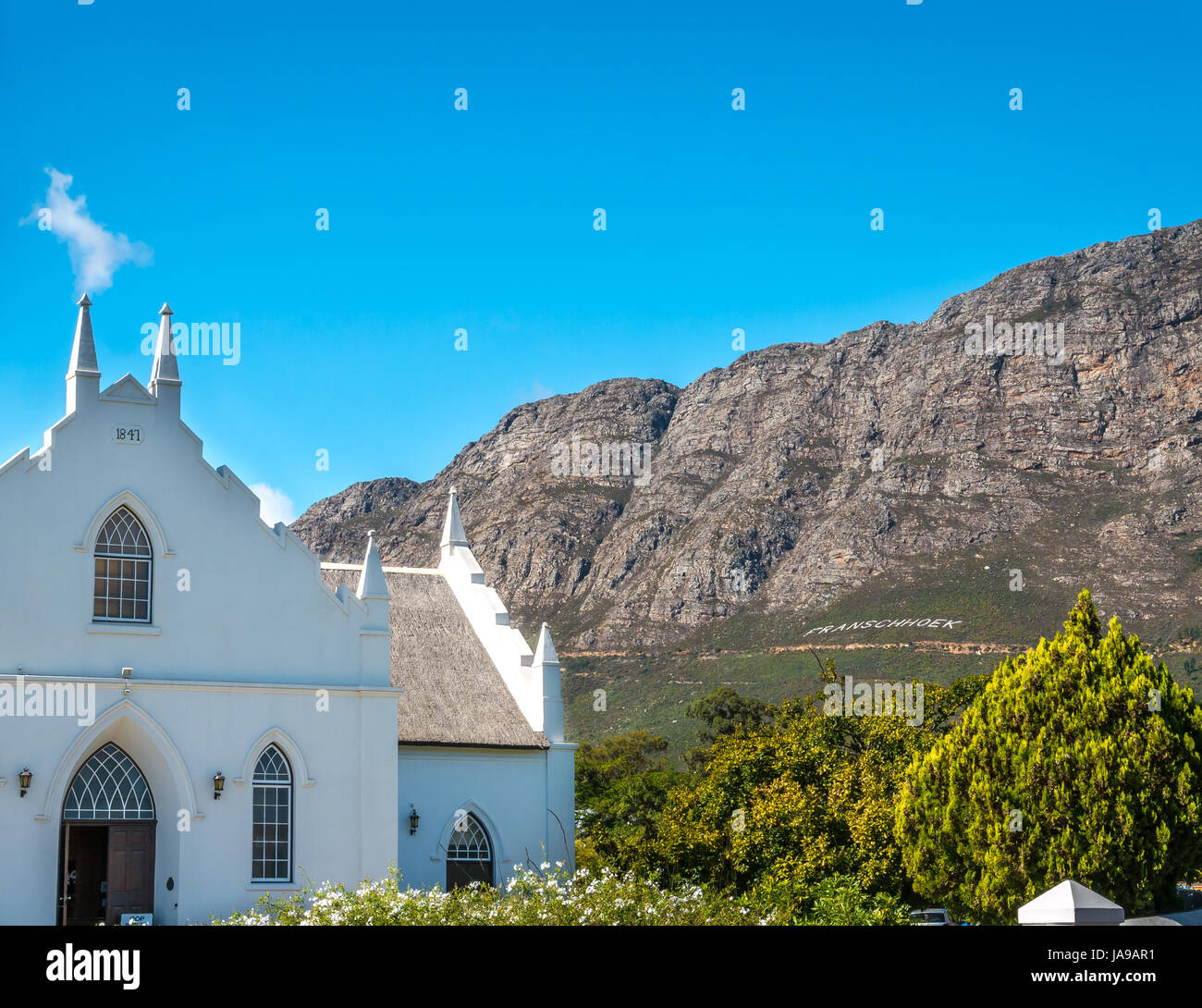 Bianco pittoresco stile Olandese del Capo chiesa, Franschhoek, Western Cape, Sud Africa, con sfondo di montagne e il cielo blu Foto Stock