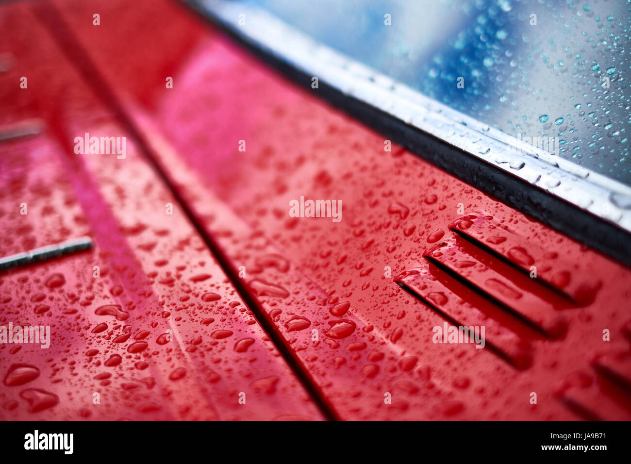 La pioggia cade su un auto rossa la formazione di gocce di acqua, close up di sfiato e finestra. Foto Stock