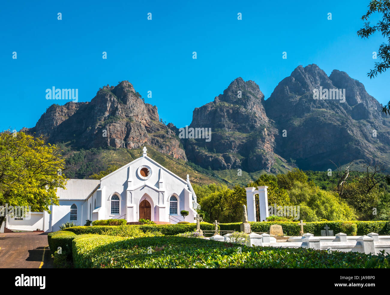 Bianco pittoresco stile Olandese del Capo chiesa, Franschhoek, Western Cape, Sud Africa, con sfondo di montagne e il cielo blu Foto Stock