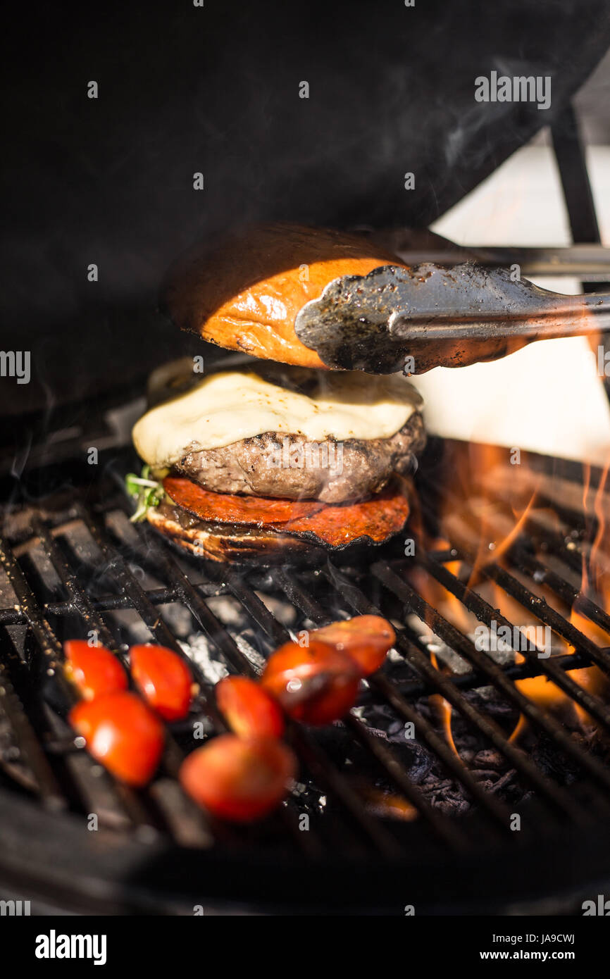 Deliziosa cheeseburger con pomodori cottura su hot flaming grill. Barbecue. Ristorante Foto Stock