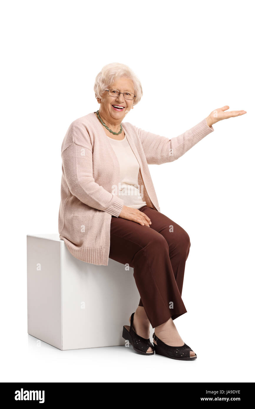 Donna matura seduto su un cubo e gesticolando con la sua mano isolati su sfondo bianco Foto Stock