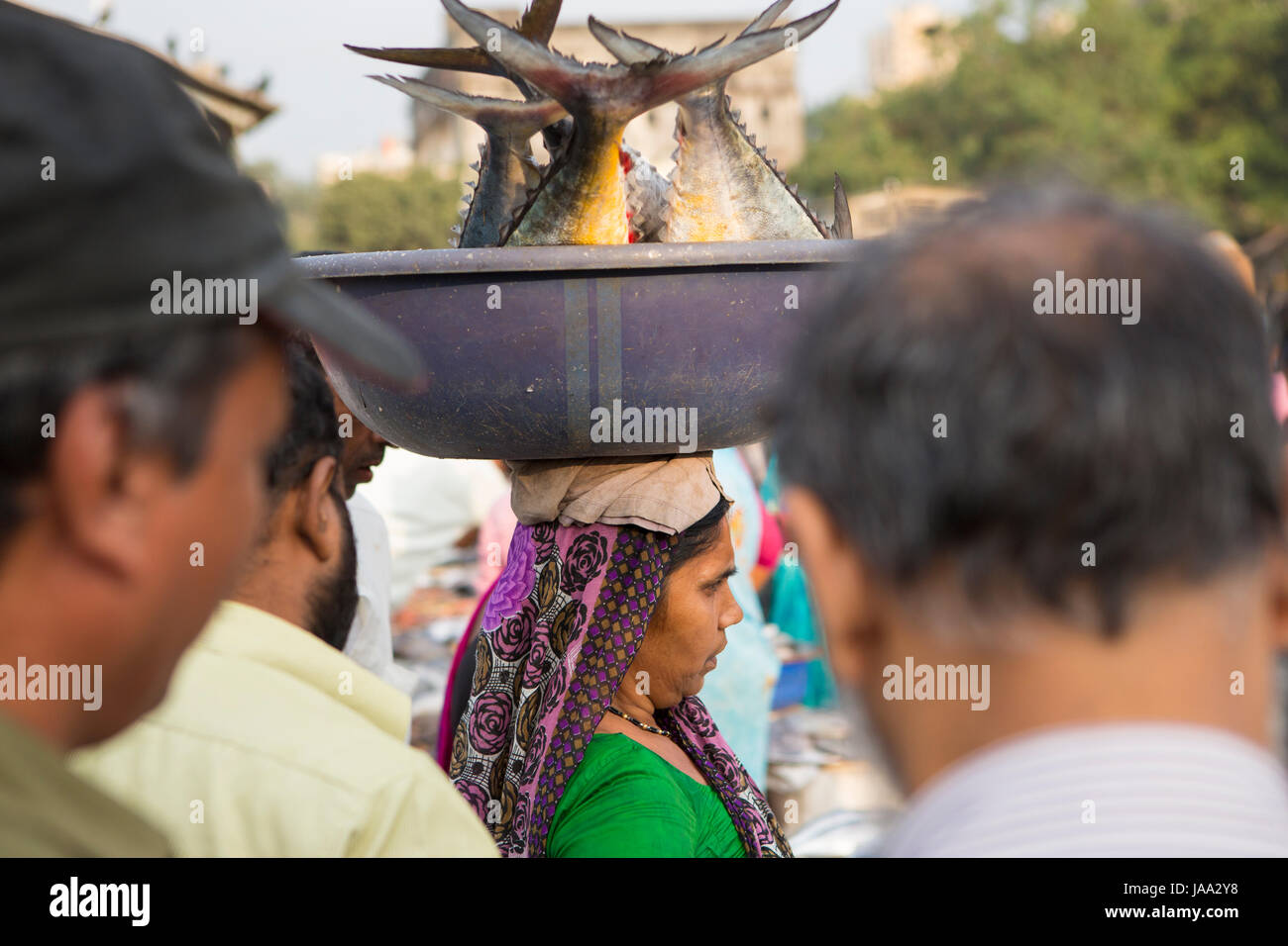 Una donna che porta quattro grandi pesci in una vasca equilibrato sul suo capo a Sassoon dock, Mumbai, India. Foto Stock
