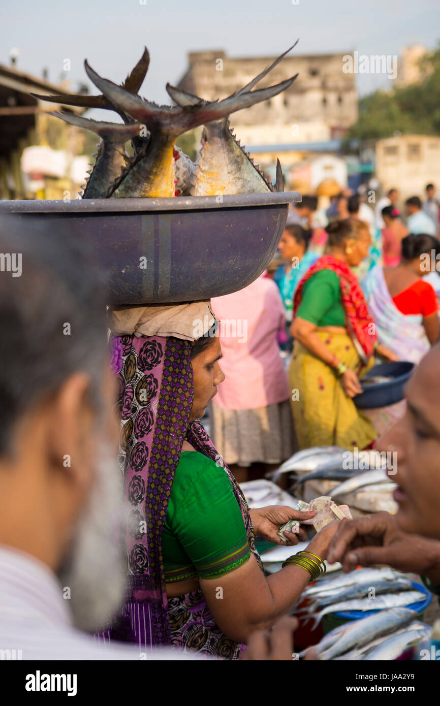 Una donna che porta quattro grandi pesci in una vasca equilibrato sul suo capo a Sassoon dock, Mumbai, India. Foto Stock