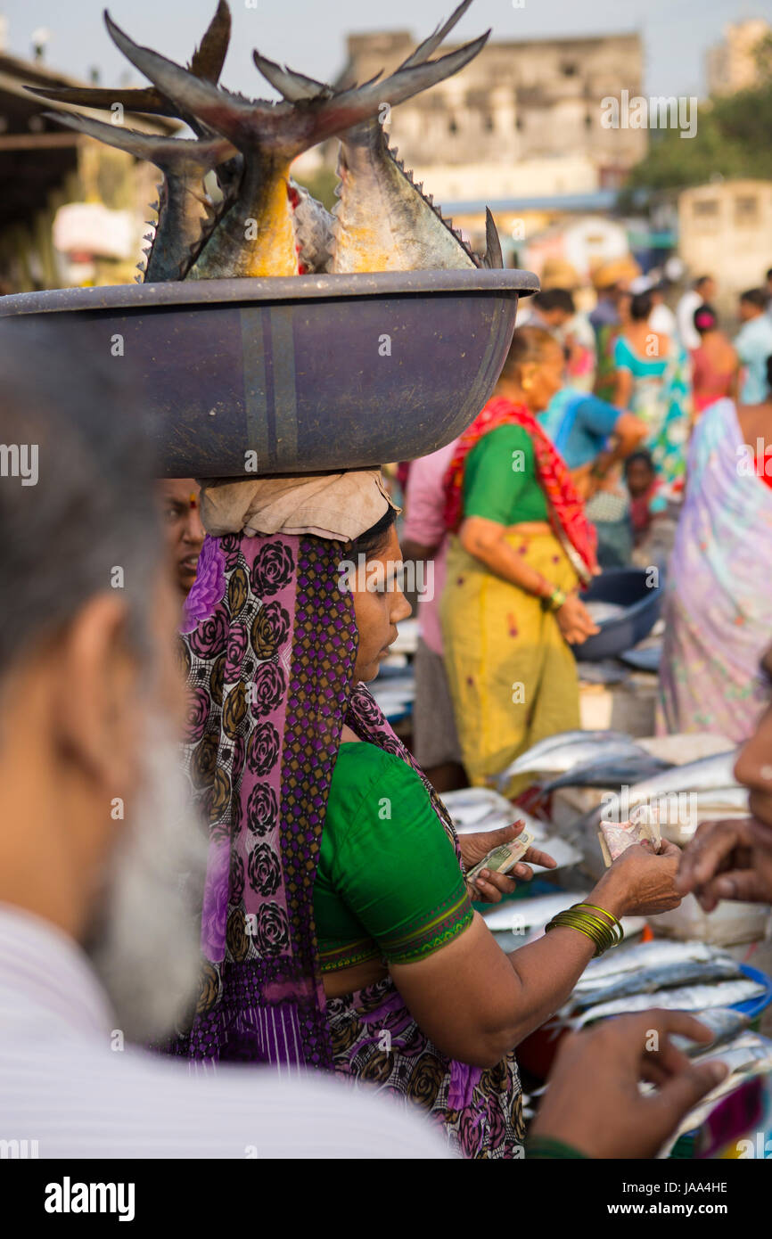 Una donna che porta quattro grandi pesci in una vasca equilibrato sul suo capo a Sassoon dock, Mumbai, India. Foto Stock