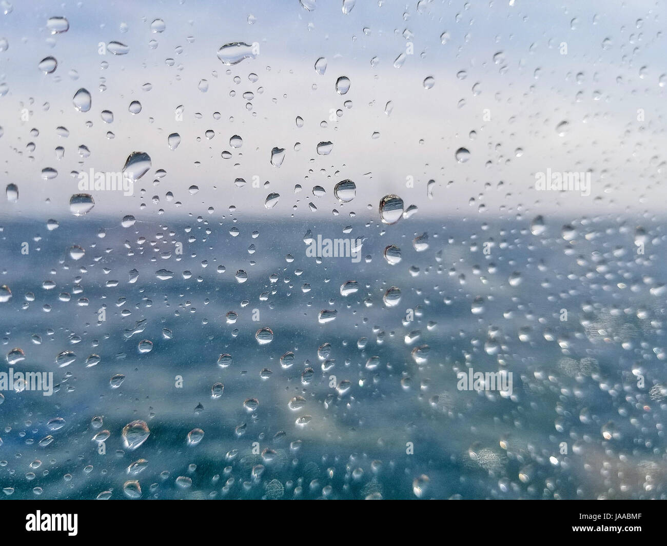 Gocce di pioggia sulla finestra con blur acqua oceanica e sfondo cielo Foto Stock