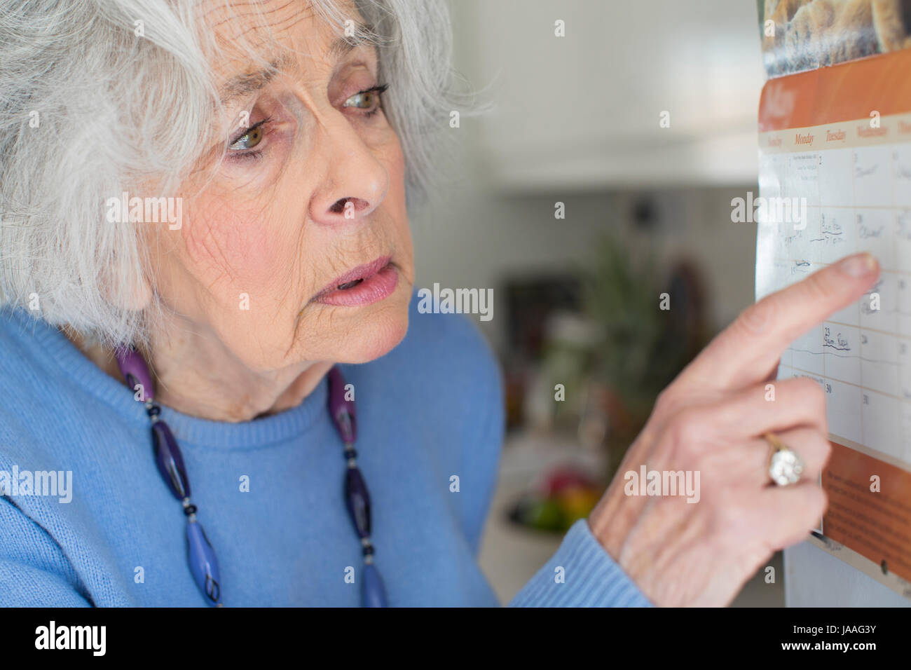 Confuso donna Senior con demenza guardando il calendario da parete Foto Stock