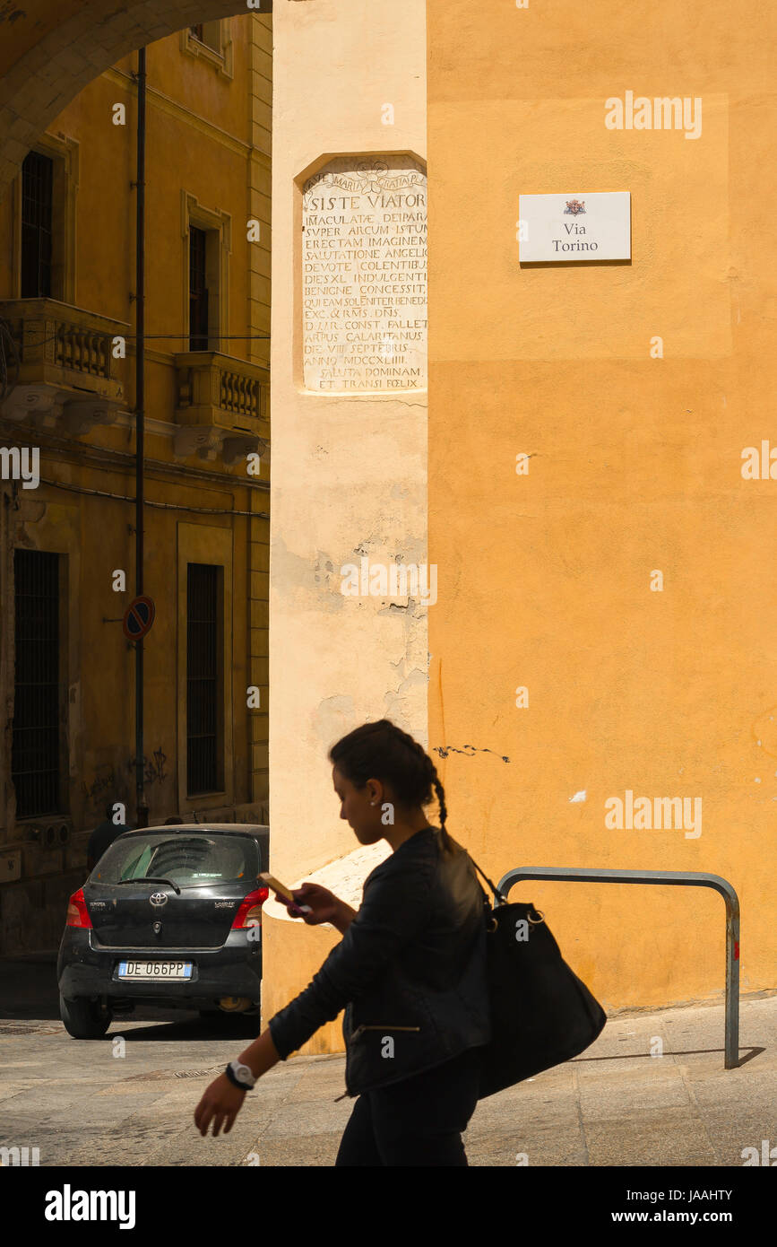 Sardegna Cagliari, mentre si verifica il suo telefono una giovane donna cammina lungo la Via Torino nel centro della città vecchia di Cagliari, Sardegna. Foto Stock