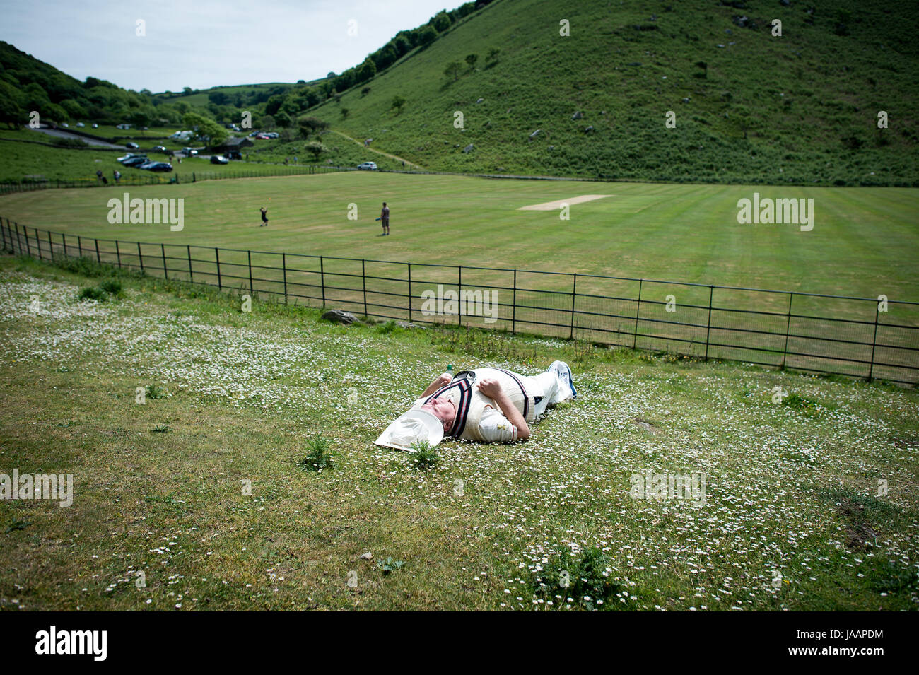 Un giocatore cattura un po' di sole prima annualmente una partita amichevole tra Cravens cavalieri e Lynton & Lynmouth Cricket Club in corrispondenza della loro base di massa all'interno della valle di rocce, North Devon. Foto Stock