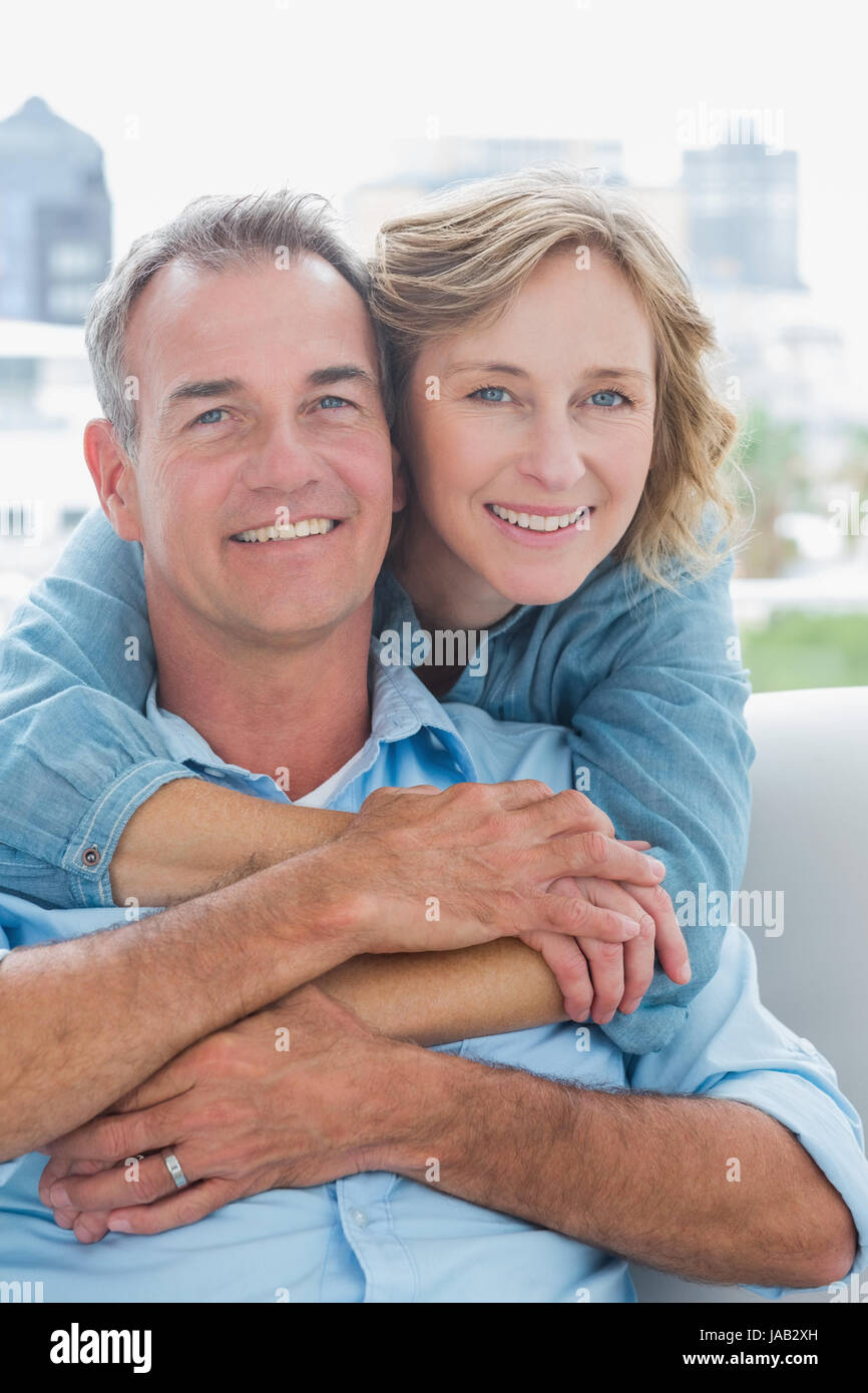 Donna felice abbracciando il marito sul lettino da dietro a casa nel soggiorno Foto Stock