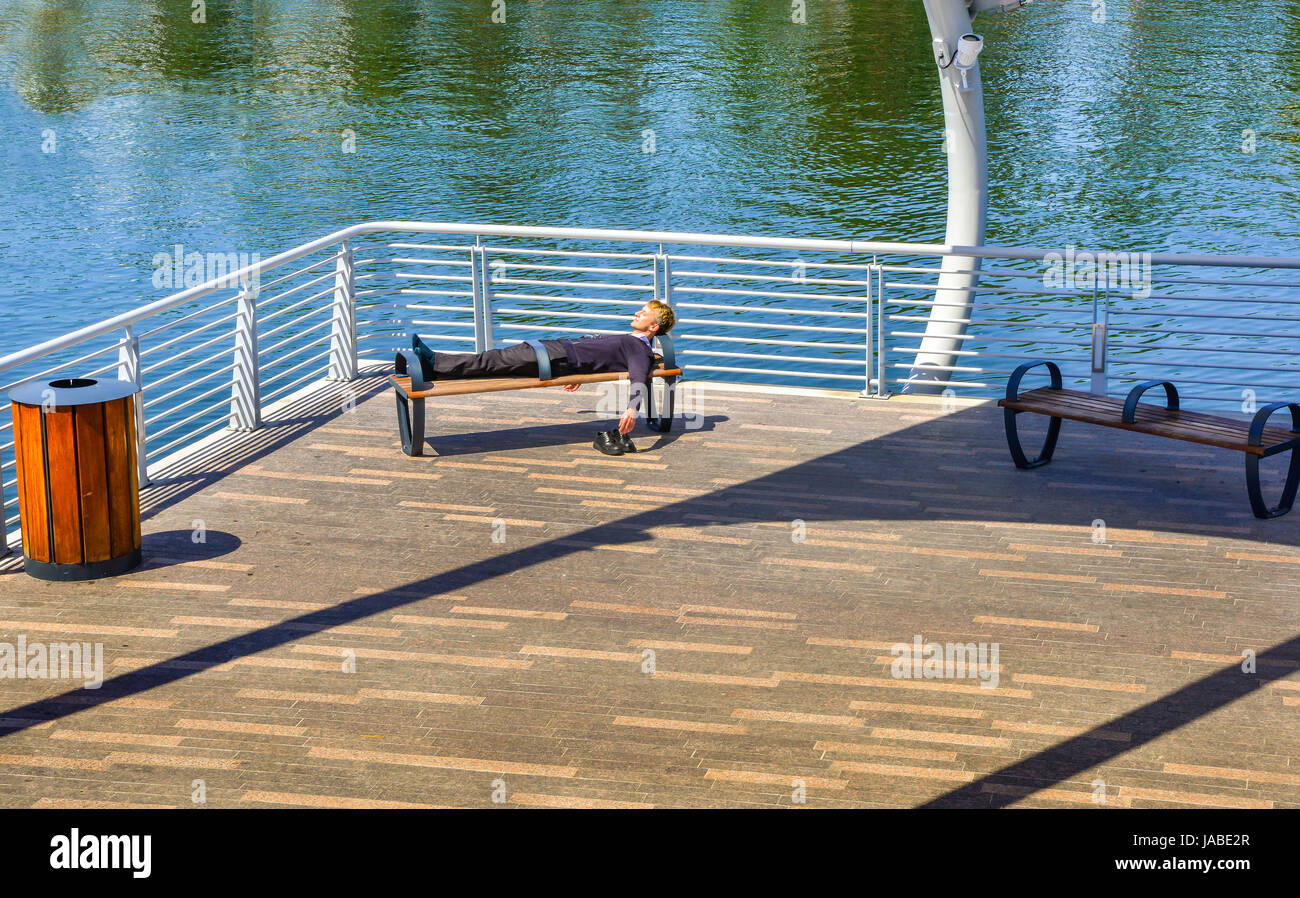 Vista dell'uomo dorme sul banco a Tampa Riverwalk del moderno design lungo il fiume Hillsborough, nei pressi del quartiere delle arti in downtown Tampa, FL Foto Stock