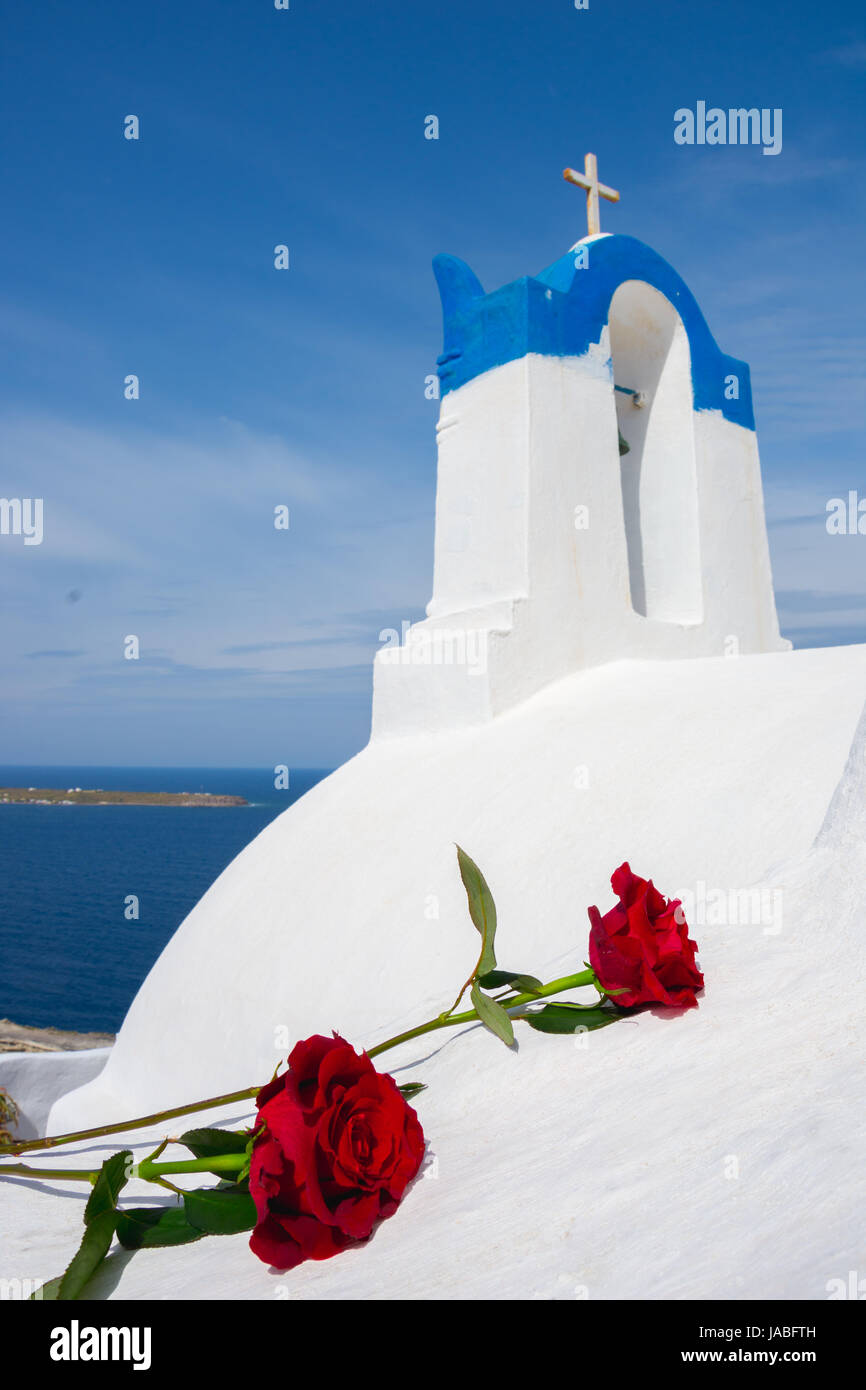 Il campanile di una chiesa ortodossa a Santorini con una coppia di rose rosse, Grecia. luna di miele estate egeo sullo sfondo delle Cicladi. Foto Stock