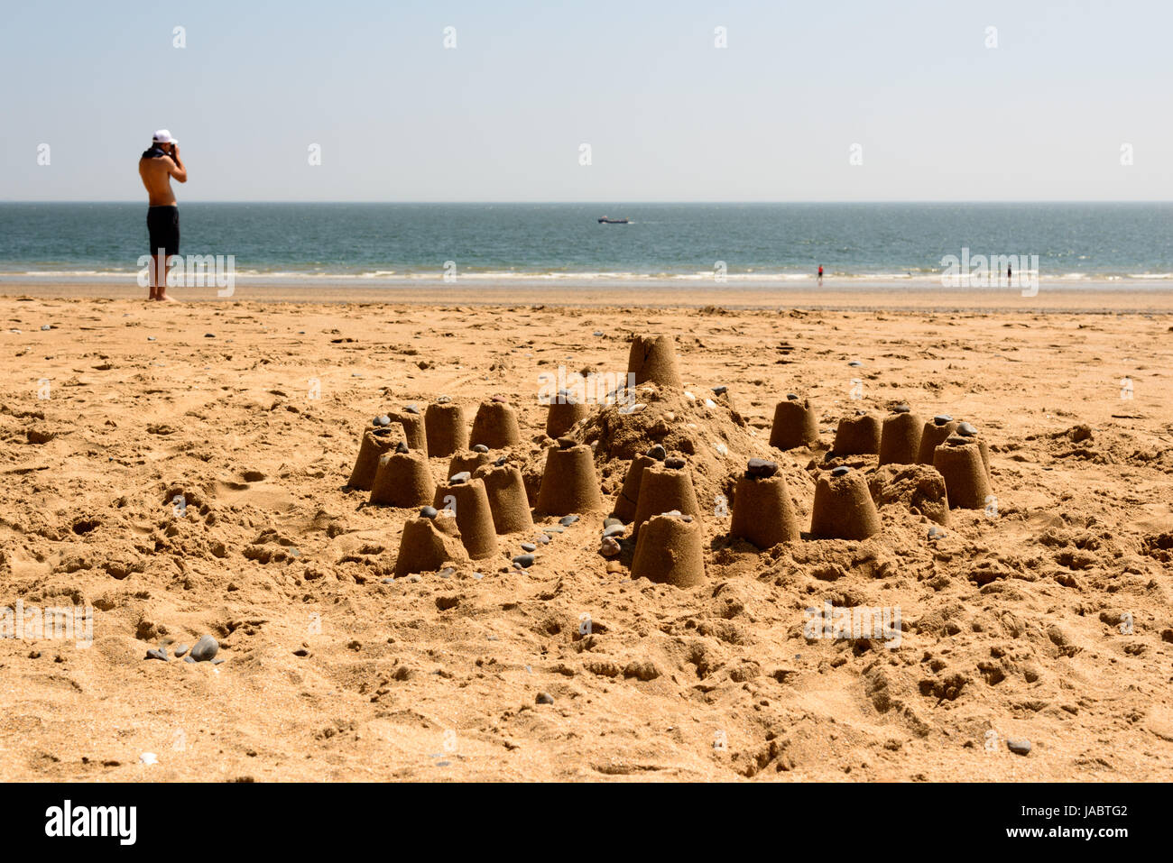 Un uomo si affaccia al mare. In primo piano, un castello di sabbia disegno sulla spiaggia. Tenby, Pembrokeshire. Regno Unito. Foto Stock