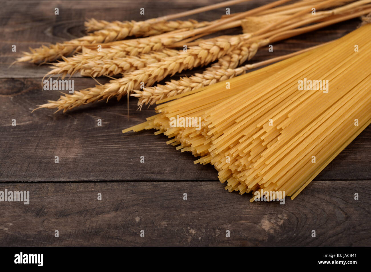 Paste alimentari non cotte e spighe di grano scuro su sfondo di legno Foto Stock