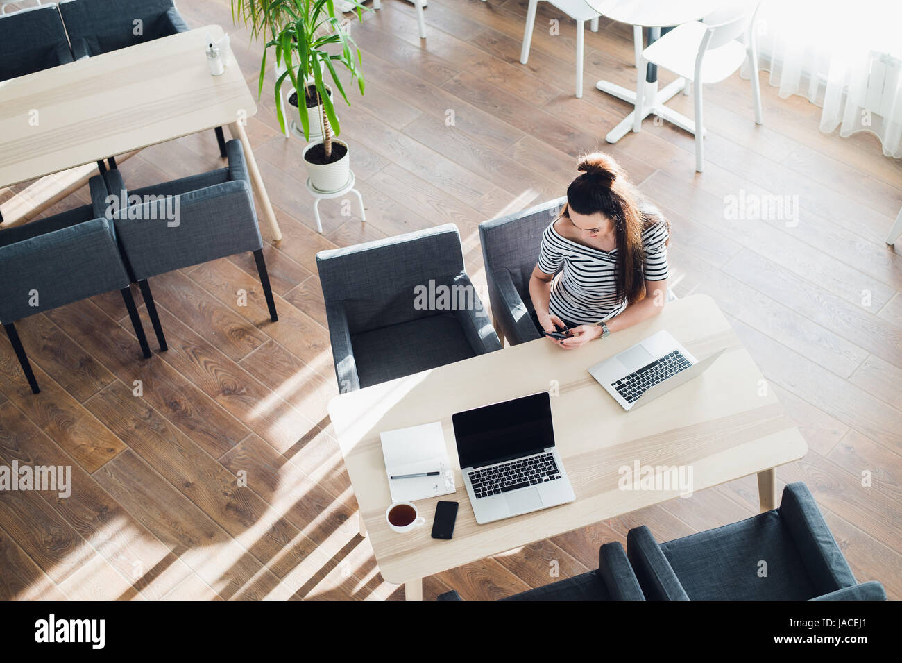 Vista superiore della femmina usando il suo computer portatile a un cafe'. Tettuccio di colpo di giovane donna seduta al tavolo con una tazza di caffè e telefono cellulare navigando in rete sul suo computer portatile. Foto Stock