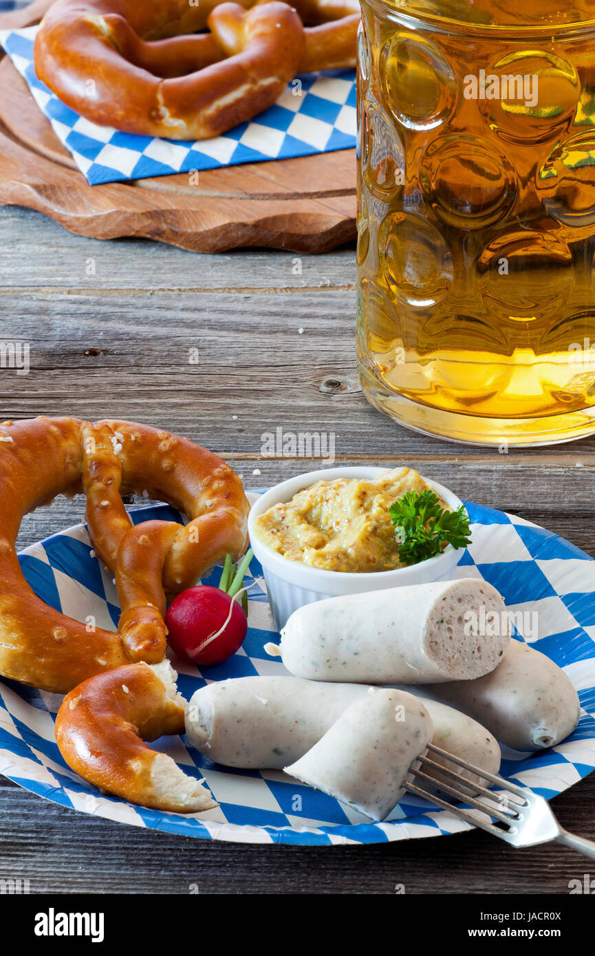 Blau-weißer Pappteller miit salsiccia bianca, Brezel, Senf und Radieschen und einem Glas mit Bier auf einem alten rustikalem Holztisch Foto Stock