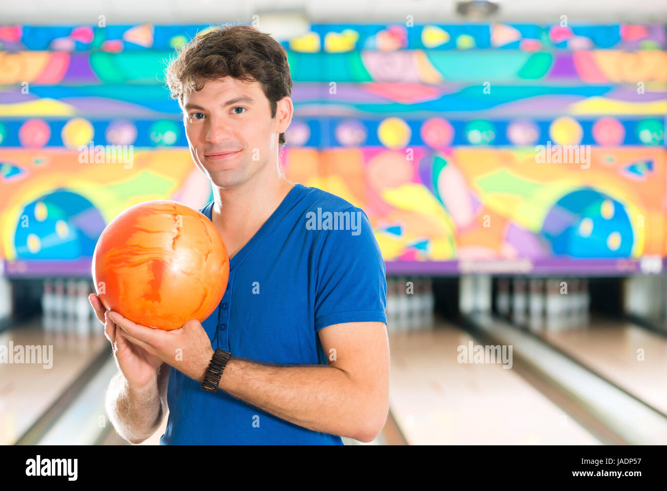 Giovane uomo in una pista da bowling avente il divertimento, l'uomo sportivo tenendo una palla da bowling di fronte alla ten pin alley Foto Stock