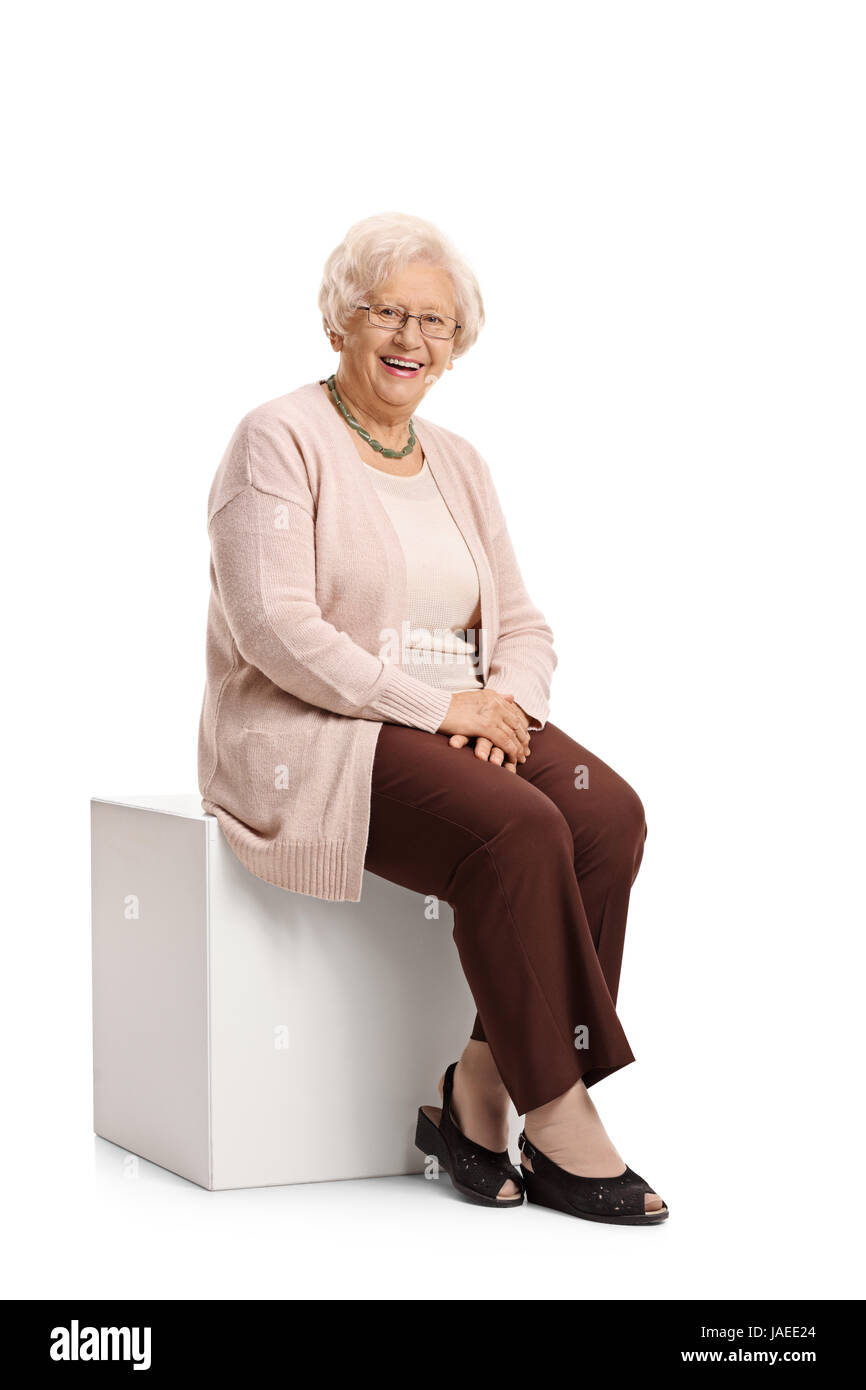 Donna anziana seduto su un cubo guardando la telecamera e sorridente isolati su sfondo bianco Foto Stock