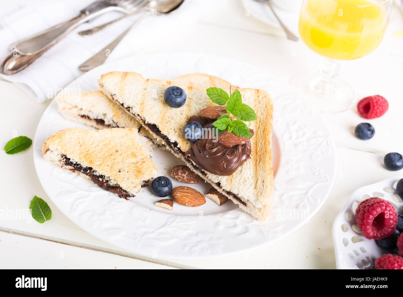 La deliziosa prima colazione con pane tostato con dado di cioccolato in pasta e bacche sul tavolo bianco. Foto Stock
