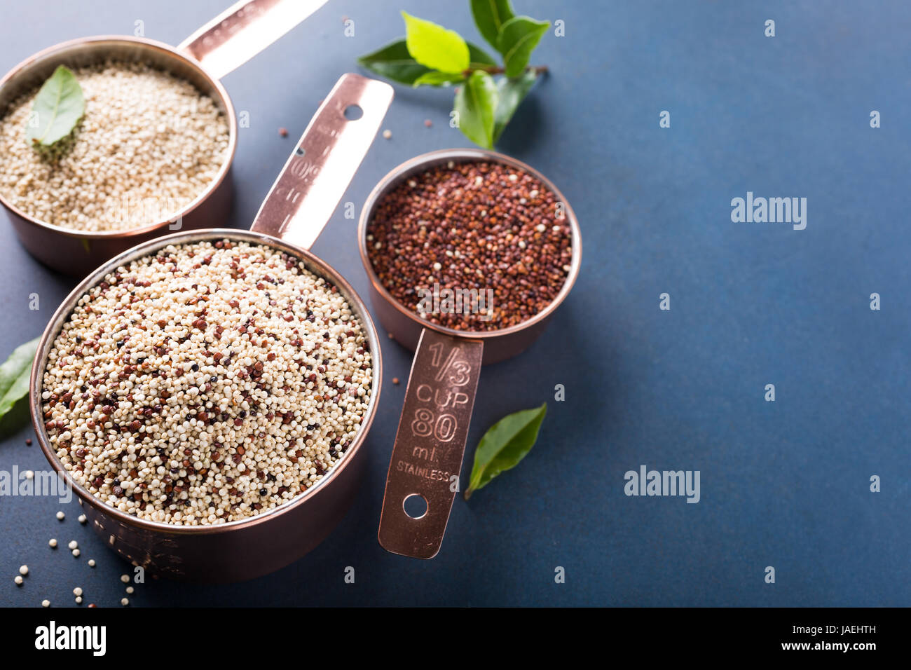 Materie miste la quinoa, sud americana di grano, nella misurazione di rame tazze di Baia con foglie di alloro su sfondo blu. Sana e prodotti senza glutine. Copia dello spazio. Foto Stock