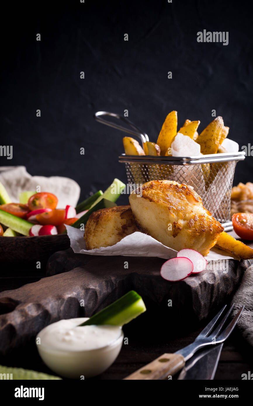 Pesce e patatine. Pesce fritto di filetto con fatti in casa di patate al forno e insalata fresca sul tagliere di legno. Foto Stock