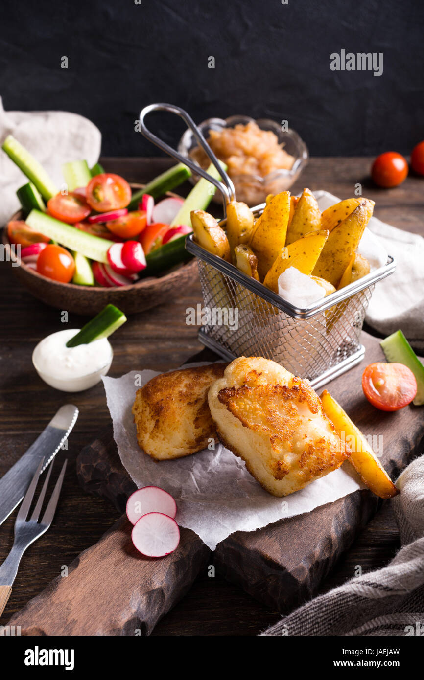 Pesce e patatine. Pesce fritto di filetto con fatti in casa di patate al forno e insalata fresca sul tagliere di legno. Foto Stock