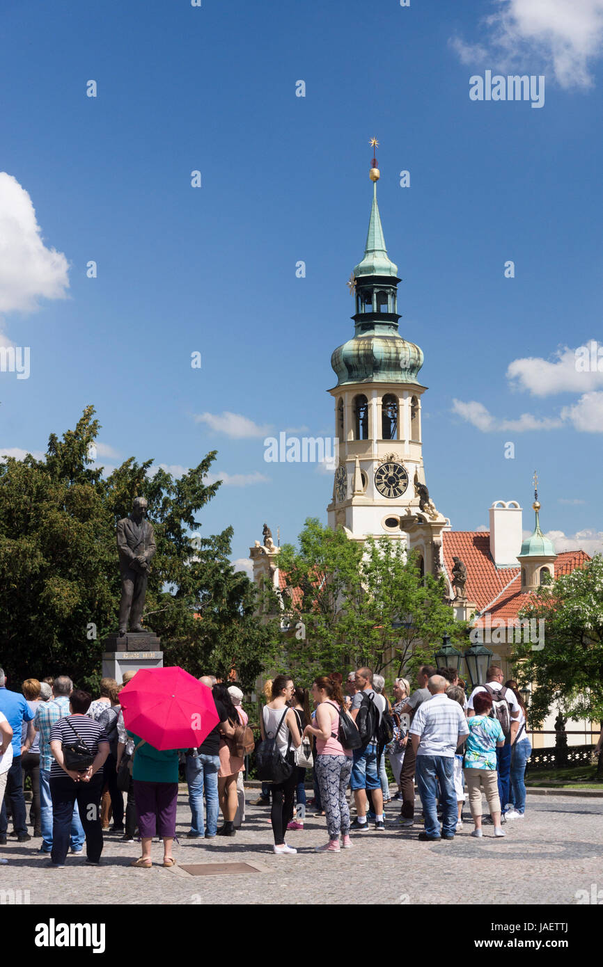 I turisti si riuniscono di fronte ad una staue di Edvard Benes, ex presidente della Cecoslovacchia. La torre dell'orologio del Loreto domina lo sfondo. Foto Stock