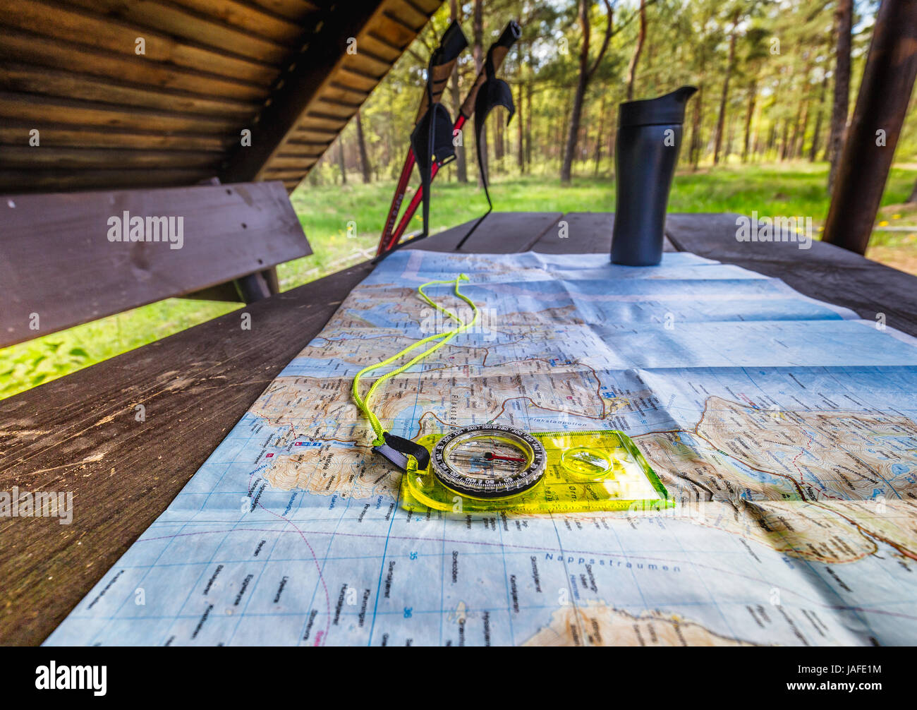 Mappa Turistica di posa su un tavolo di legno con giallo comapss su di esso. In Sfondo tazza termica e bastoncini da trekking. Foto Stock