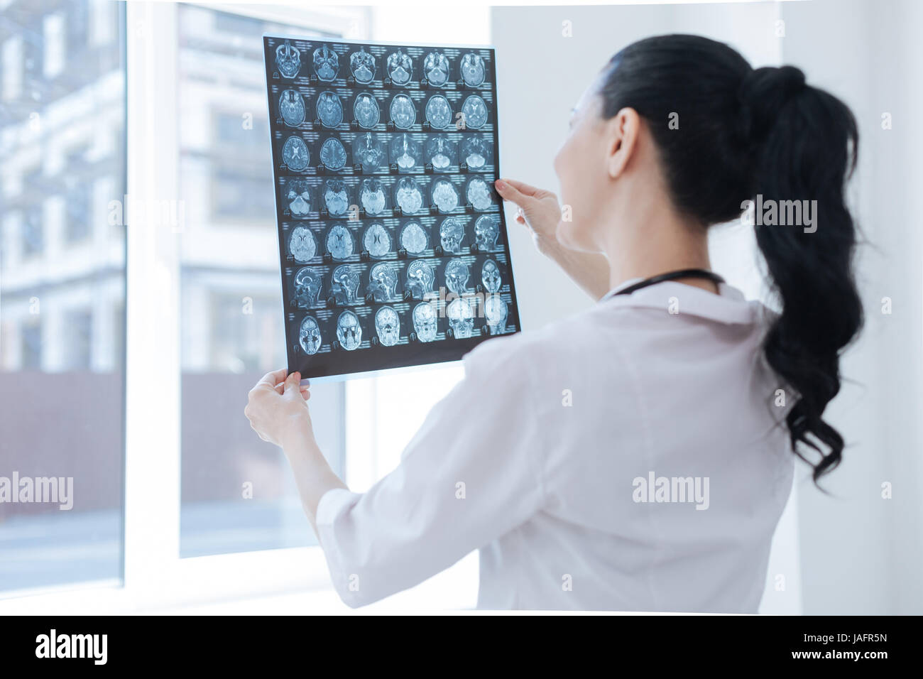 Piena di attenzioni. Ottimista attento coinvolti radiologo lavorando presso la clinica mentre esaminando il cervello x ray immagine e il rilevamento dei problemi Foto Stock