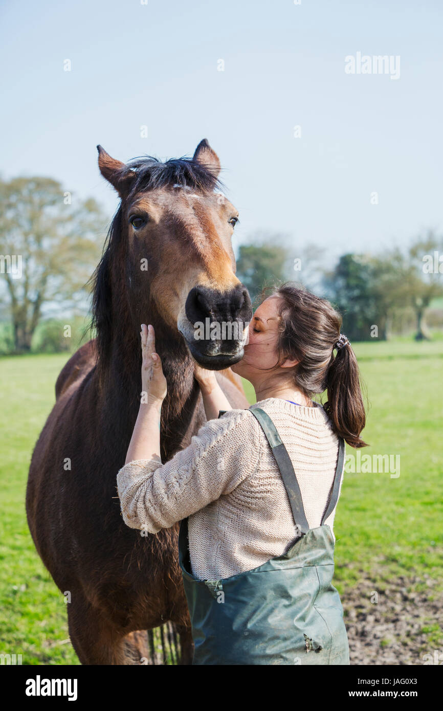 Donna in piedi all'aperto, baciando un cavallo marrone sulla guancia. Foto Stock
