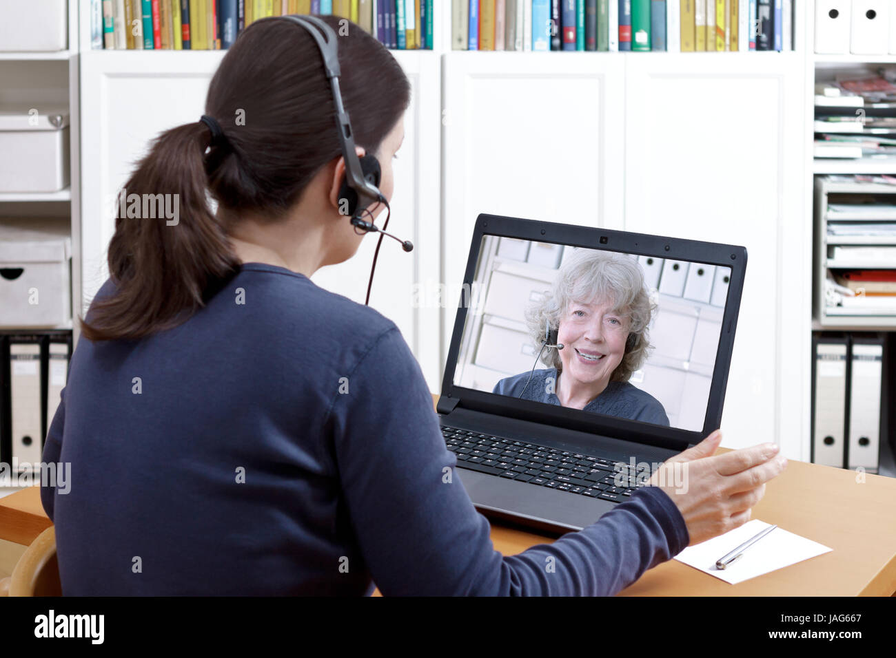 Donna con cuffie alla sua scrivania davanti al suo computer portatile avente una chat video con la sua nonna felice, lo spazio di testo Foto Stock