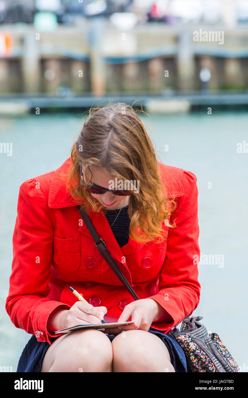 Donna che scrive cartoline seduto sul porto a Weymouth, Dorset UK nel mese di giugno Foto Stock