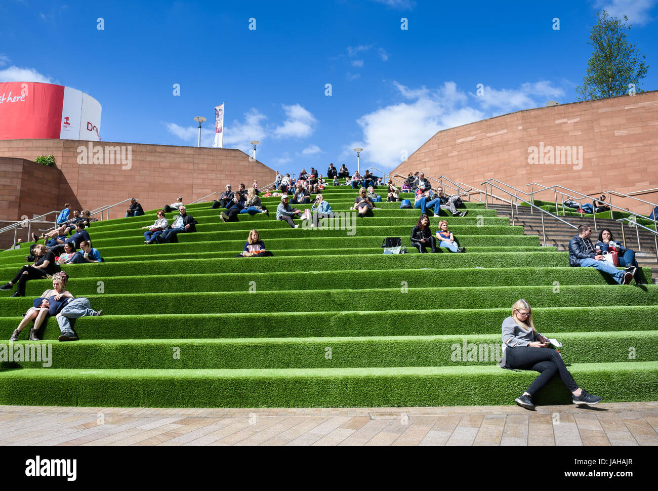 I giovani seduti al sole sui passi nelle vicinanze del Liverpool One Shopping Centre in Merseyside Foto Stock