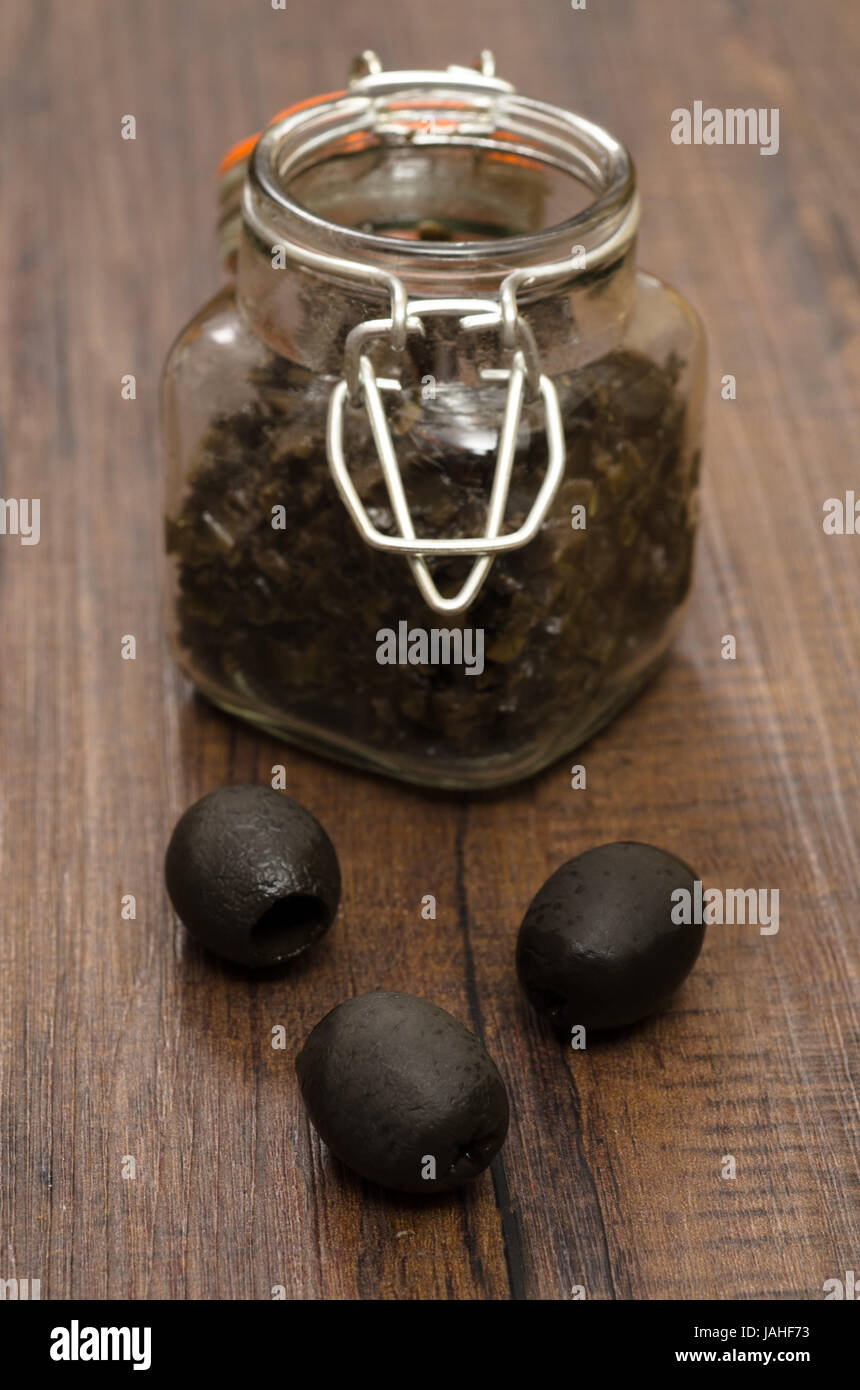 Schwarze Oliven und Tapenade im Glas im Hochformat Foto Stock