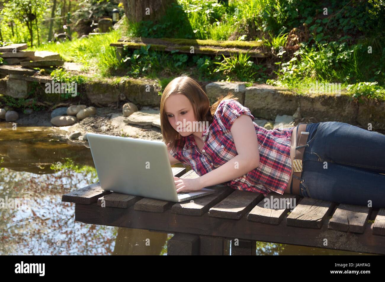 Frau liegt am Gartenteich und surft mit ihrem Laptop Foto Stock