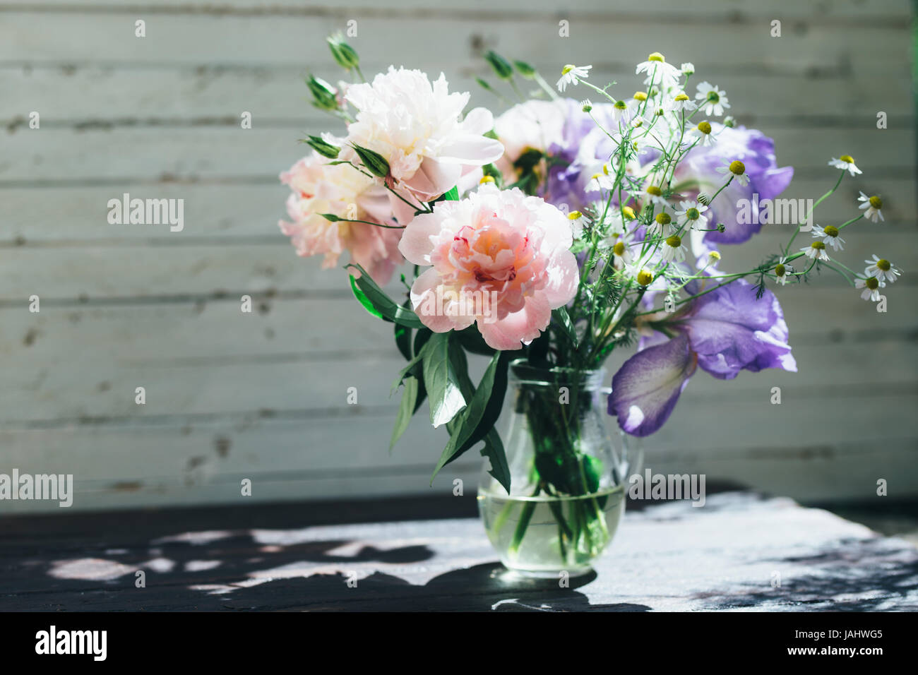 Bouquet di peonie bianco, chamomiles e iride fiori in vaso di vetro. Estate sfondo. Foto oscurata Foto Stock