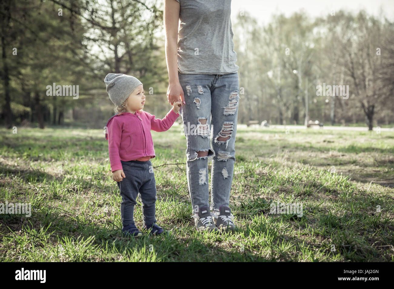 Bambino con sua madre camminare insieme con tenendo le mani in estate park sull'erba. Tema principale è il bambino. Irriconoscibile madre sulla foto. Concetto per tog Foto Stock