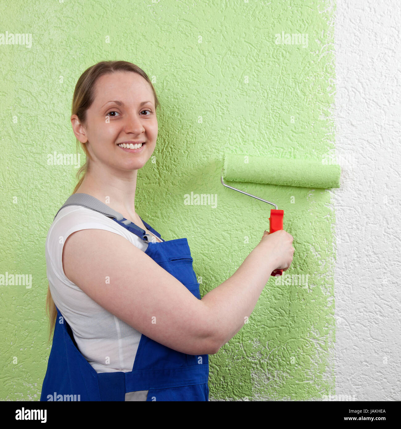 Eine lachende Frau streicht eine Wand mit einer Farbwalze Foto Stock