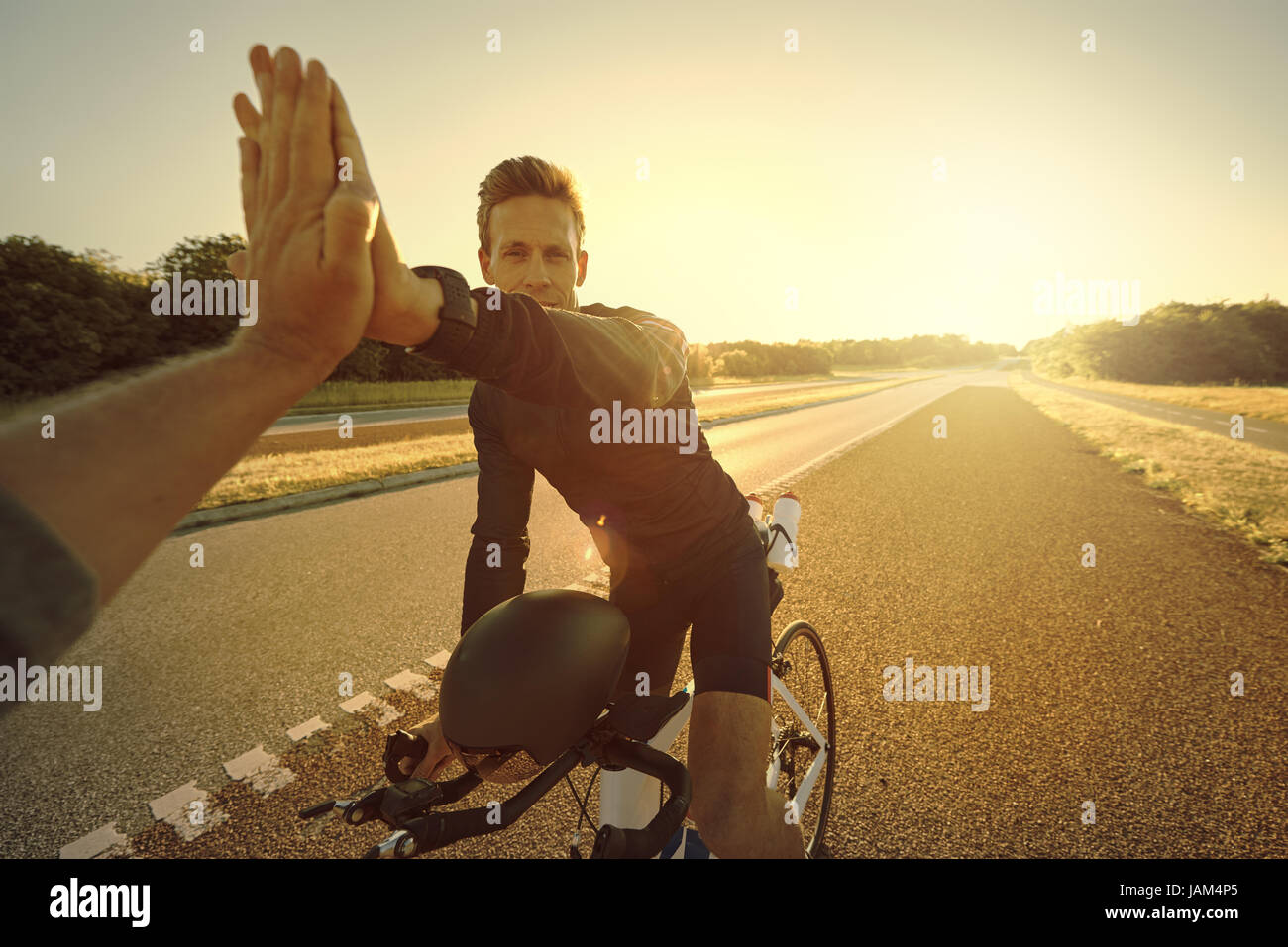 Montare sportive persona sulla bicicletta professionale dando un alto cinque sull'autostrada vuota in serata. Foto Stock