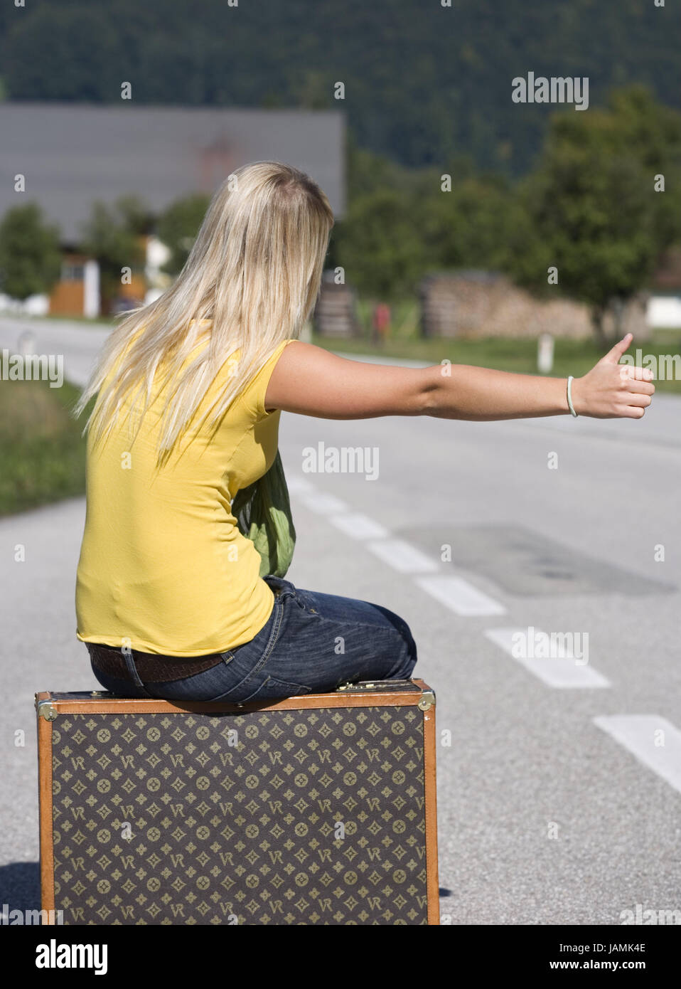 Strada,adolescente,ragazza,valigia,sit,strappare autostopping,street,la segnaletica stradale,persona,vista posteriore,bionda,T-shirt,giallo,jeans,bagagli,corsa,avventura,libertà,BRACCIO,mano,pollex,punto,gesto,personaggio,attendere, Foto Stock