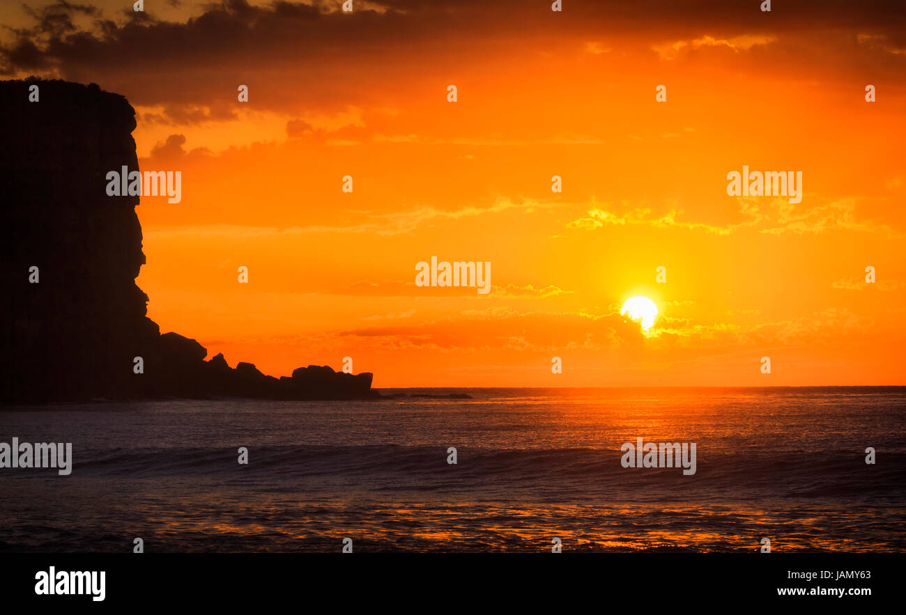 Arancio luminoso rosso il sorgere del sole attraverso le nuvole oltre oceano Pacifico orizzonte off Avalon Beach a nord di Sydney. Ocean superficie riflette la luce solare. Foto Stock