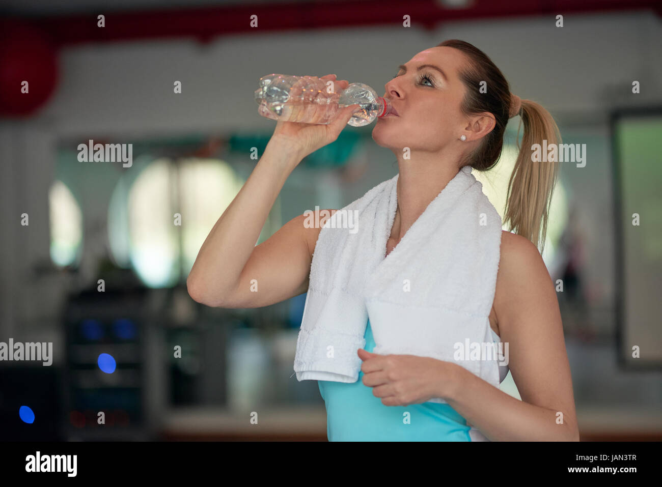 Donna di mezza età atleta di bere acqua in bottiglia per l'idratazione dopo gli allenamenti in palestra in una salute e concetto di fitness Foto Stock
