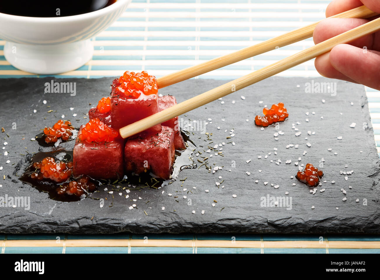 Tonno sashimi immerso in salsa di soia con salmone roe, spessa sale e aneto su pietra ardesia con bacchette e ciotola con semi di soia. Pesce crudo in Japane tradizionali Foto Stock