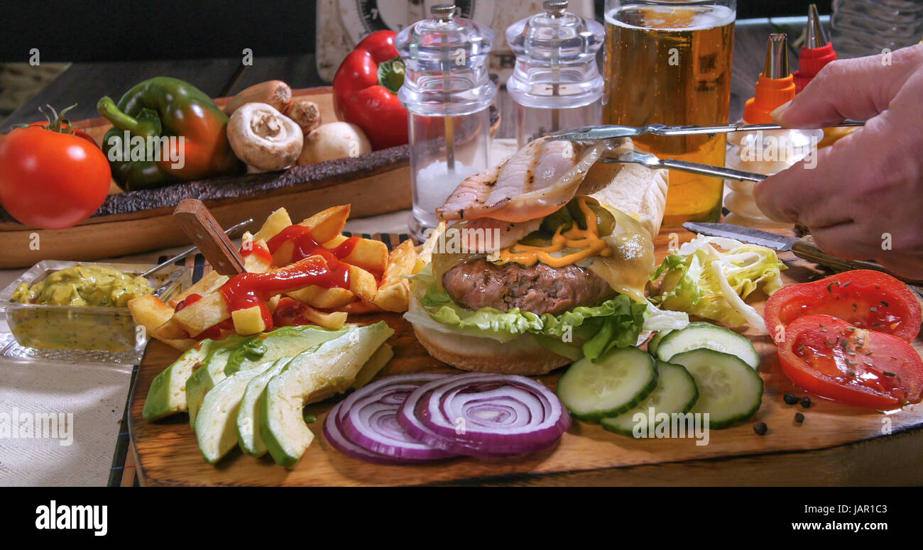 Aggiunta di bacon croccante su una deliziosa cheesburger con birra e patatine fritte Foto Stock