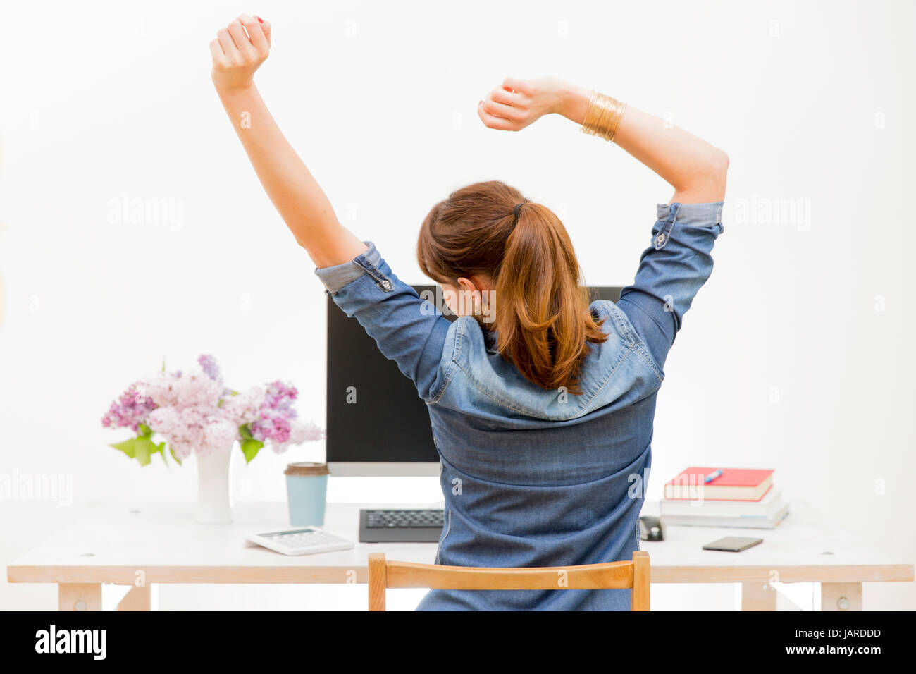 La donna lo stiramento delle sue braccia seduta al tavolo di lavoro accanto al computer Foto Stock