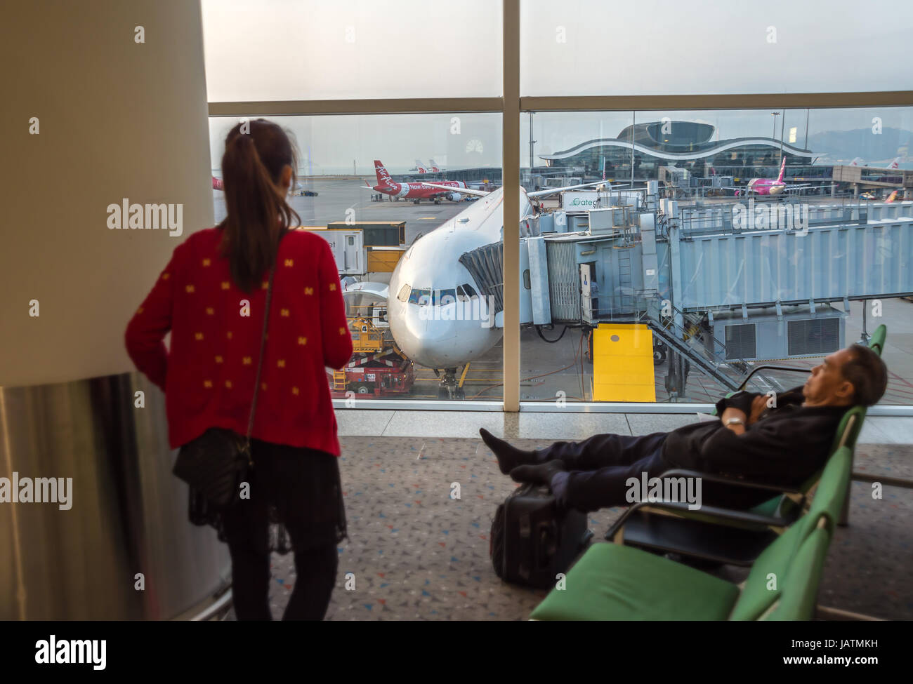 Hong Kong, Cina, 28 febbraio 2015. due passeggeri asiatici in attesa del loro volo con un piano in background Foto Stock