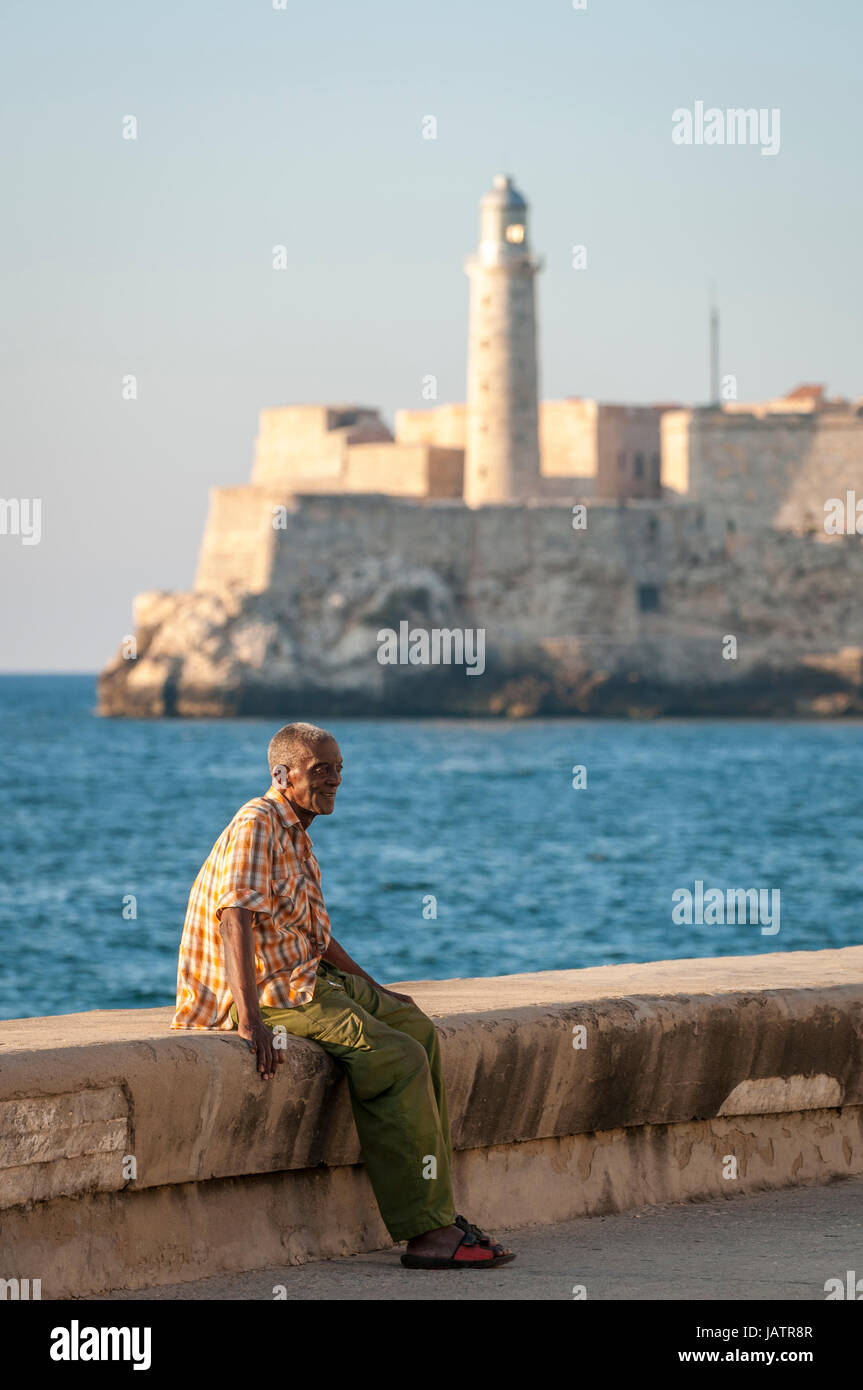 L'Avana, Cuba - circa maggio, 2011: Anziani uomo cubano si rilassa sulla parete di Malecon con il Morro faro in background. Foto Stock